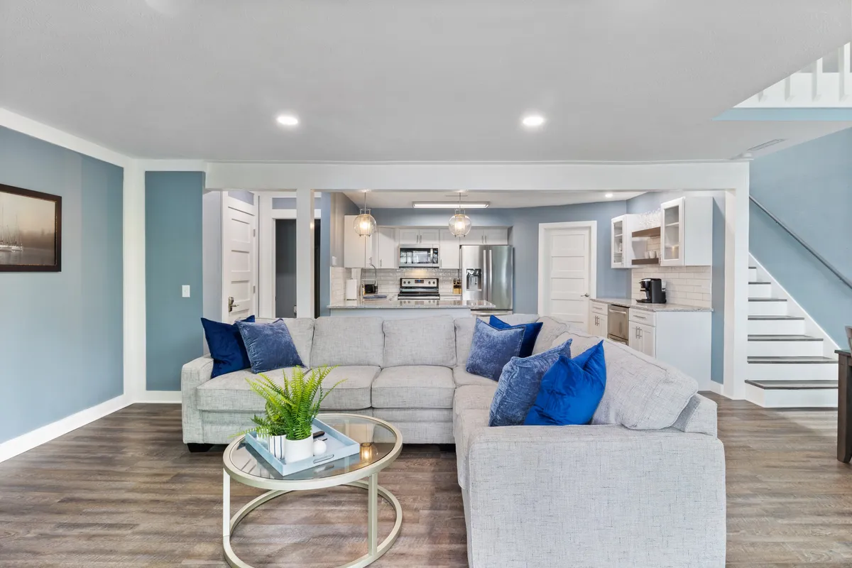 A spacious living area featuring a large sectional sofa and a coffee table, with the kitchen visible in the background. The open-concept layout hints at communal activities like socializing, movie nights, and entertaining guests.