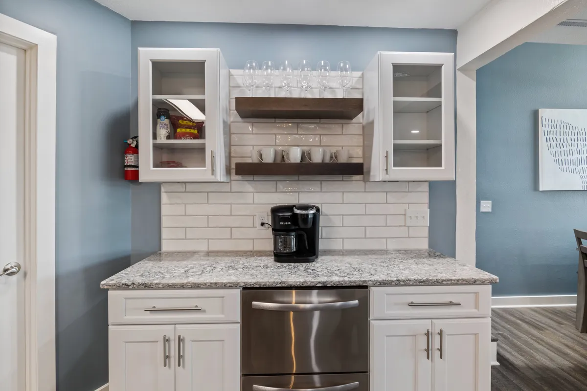 A close-up of a kitchen coffee station, with a coffee maker, cabinetry, glassware, and granite countertop. The setup is perfect for enjoying a fresh cup of coffee or prepping for a casual brunch, adding a lived-in, welcoming touch to the kitchen environment.