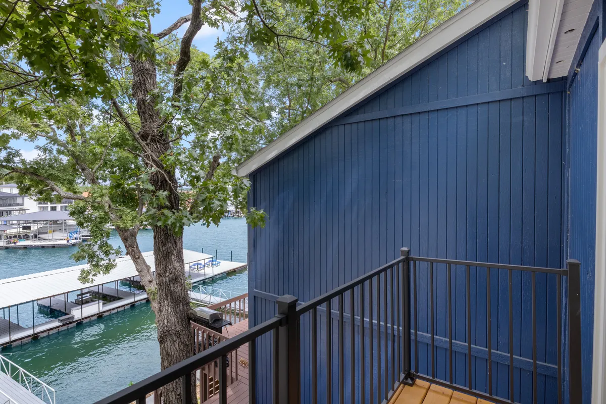 The image features a tranquil dock area with dark blue wooden siding, tree foliage, and the water's surface visible alongside the dock. The setting is calm and inviting, suggesting a place perfect for waterfront relaxation and activities.