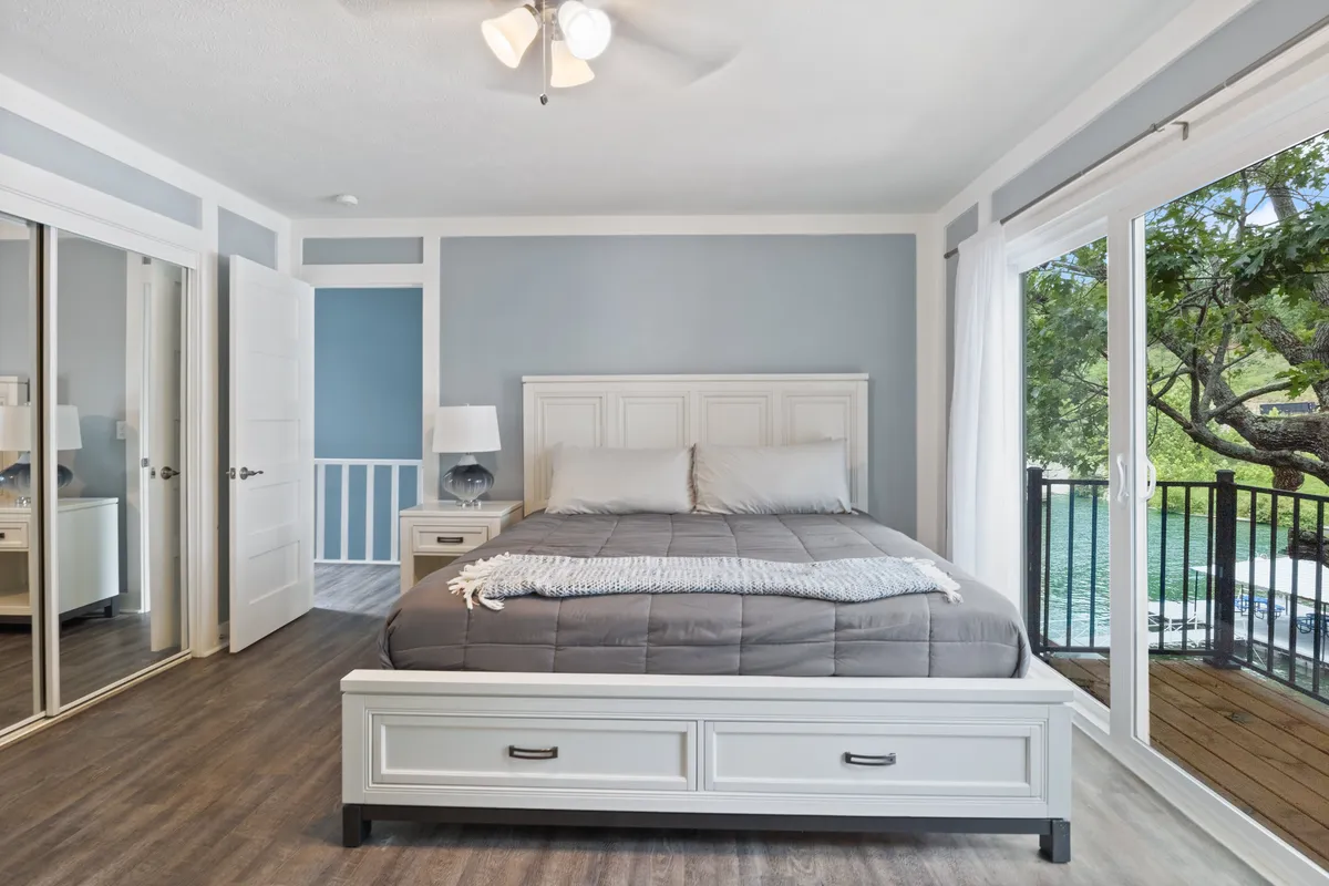 A serene bedroom featuring a plush bed adorned with soft linens, large window letting in natural light, nightstands on each side, and a mirror adding depth to the space. The tranquil décor, with muted tones and minimal clutter, creates an inviting atmosphere for deep rest and relaxation.