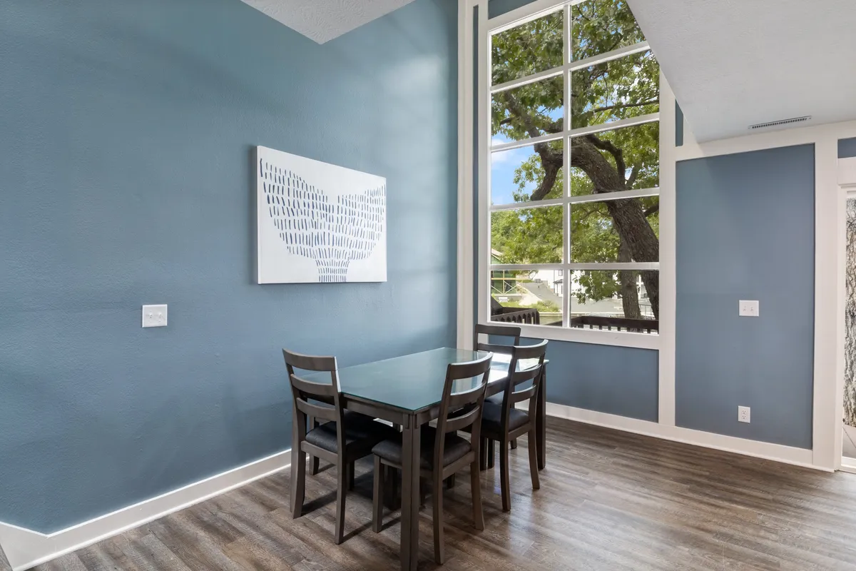 A dining area with a contemporary table, large window, and wall art. The space is designed for relaxed meals, socializing, or celebrations, and is directly adjacent to the kitchen, making it easy for the cook to stay part of the action.