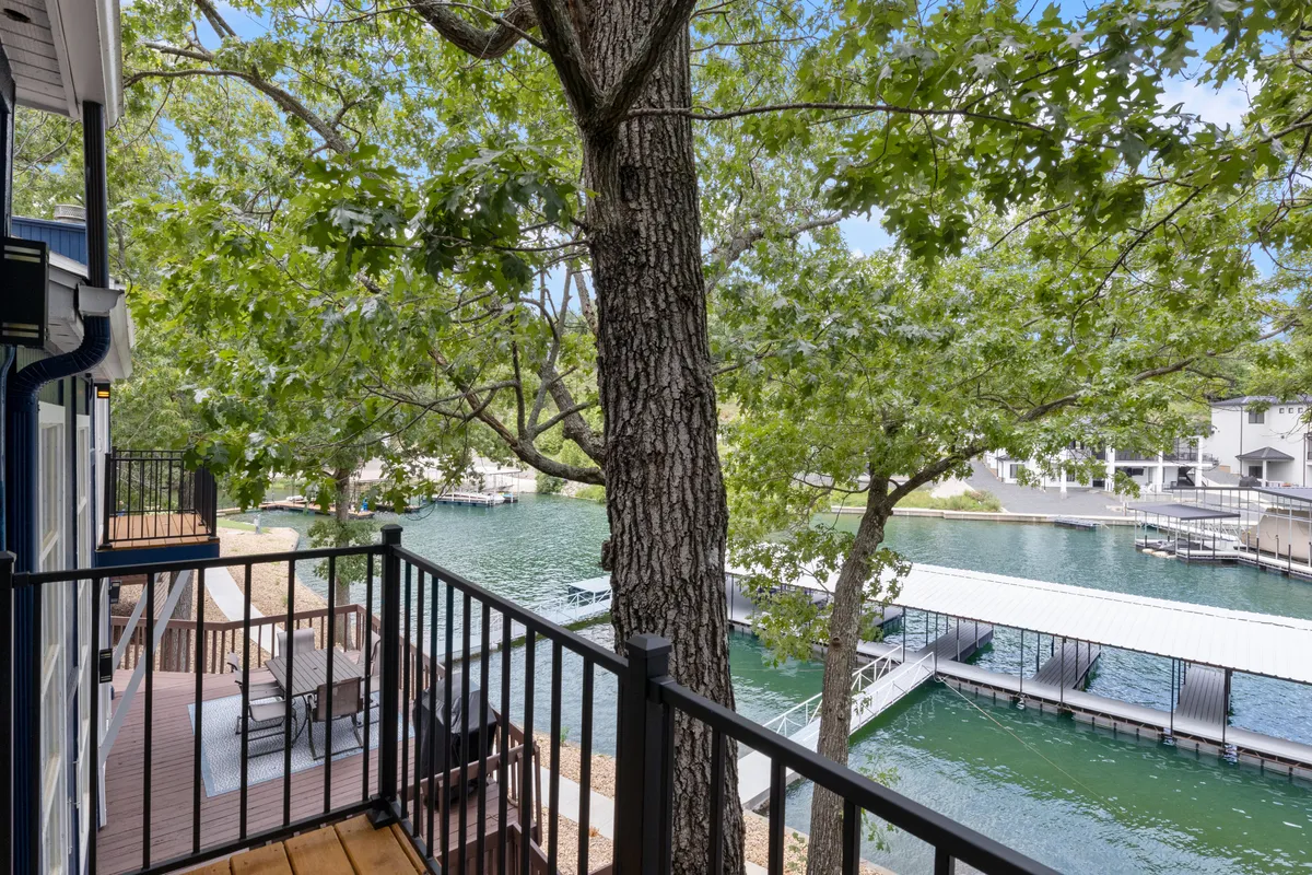 This image displays a peaceful waterfront with a dock, tree coverage, and comfortable balcony seating overlooking the water. The dock is clearly visible, emphasizing access to the water and leisure possibilities.