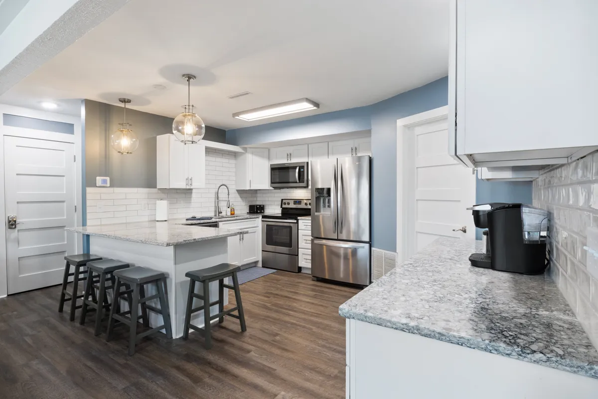 A bright, modern kitchen featuring a central island with granite countertops, stainless steel appliances, pendant lighting, and ample space for meal prep. The inviting setup is perfect for socializing, cooking, or entertaining guests, with bar seating at the island inviting friends and family to gather.